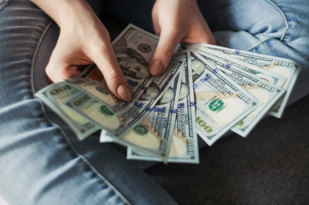 Person holding a fanned-out stack of one-hundred-dollar US bills