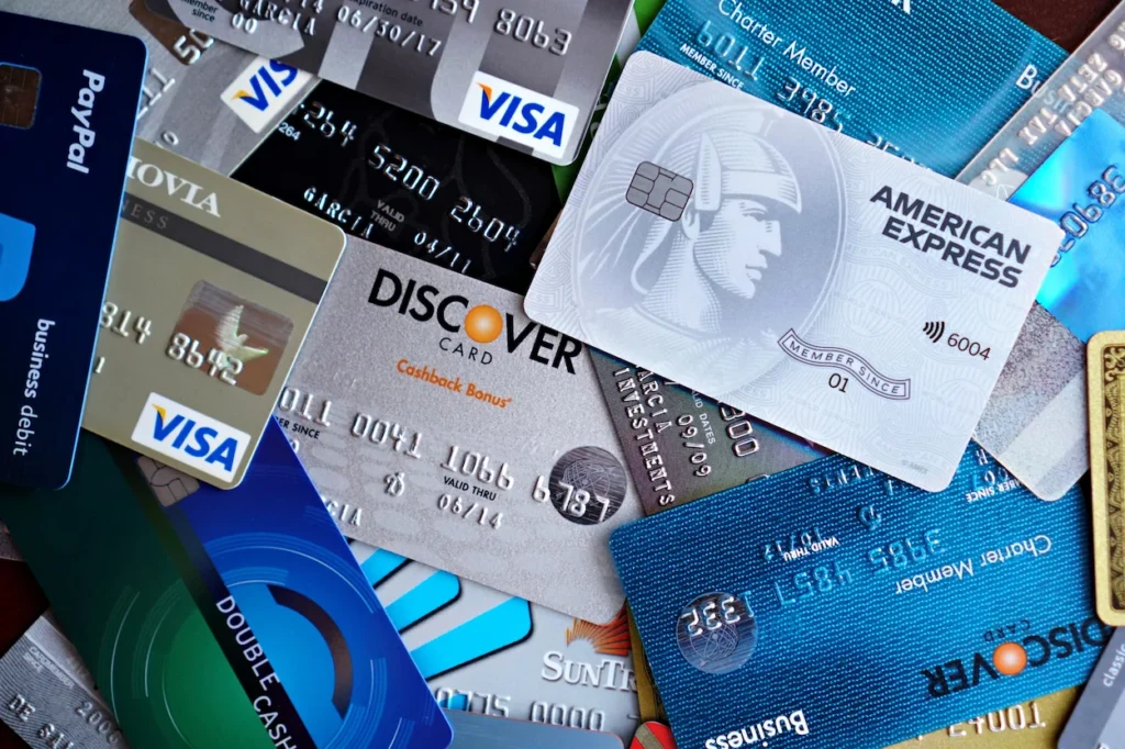 A scattered pile of multiple bank credit cards featuring logos for Visa, Discover, and American Express