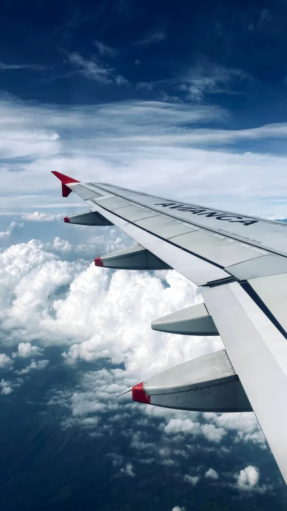 Avianca airplane wing with red winglets flying above fluffy white clouds
