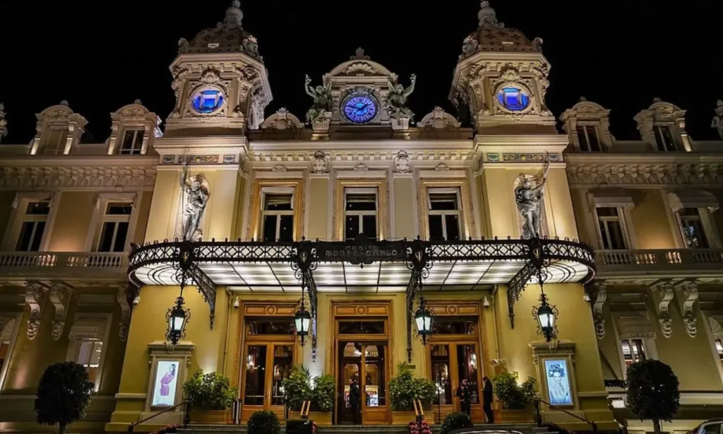 The Casino de Monte Carlo glows with elegant lights against the night sky.