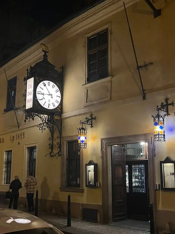 The historic U Fleků building at night with its large clock and illuminated lanterns.