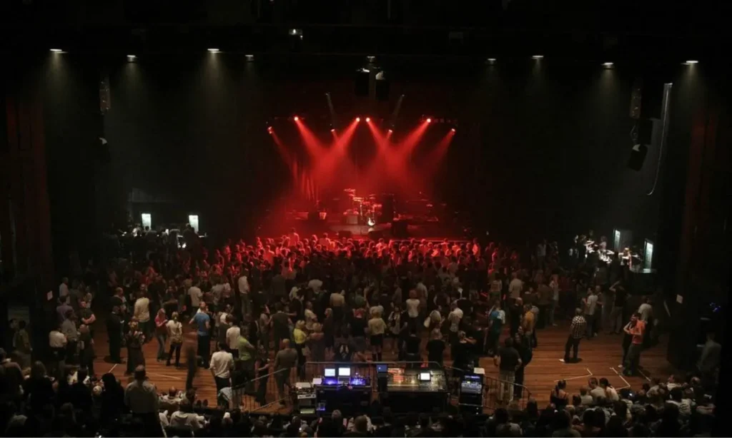 A crowd gathers under red stage lights at Melkweg for a concert.