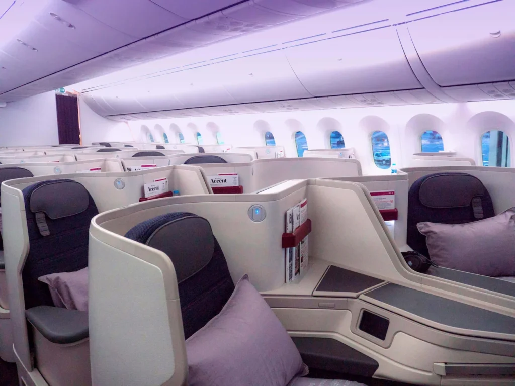 Modern white business class seats with dark gray upholstery and purple pillows inside an airplane