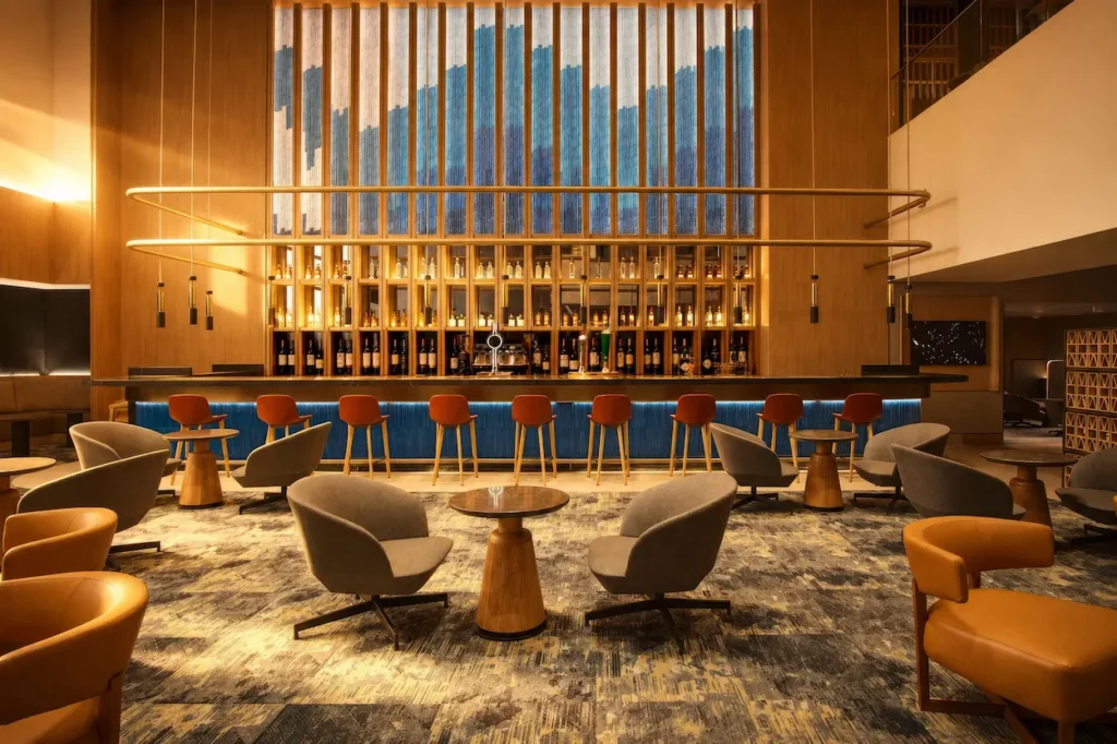 A luxury airport lounge bar featuring contemporary wooden paneling, a blue backdrop, and plush modern armchairs