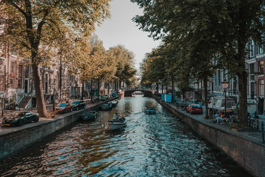 Small boats cruising down a tree-lined Amsterdam canal bordered by historic brick houses