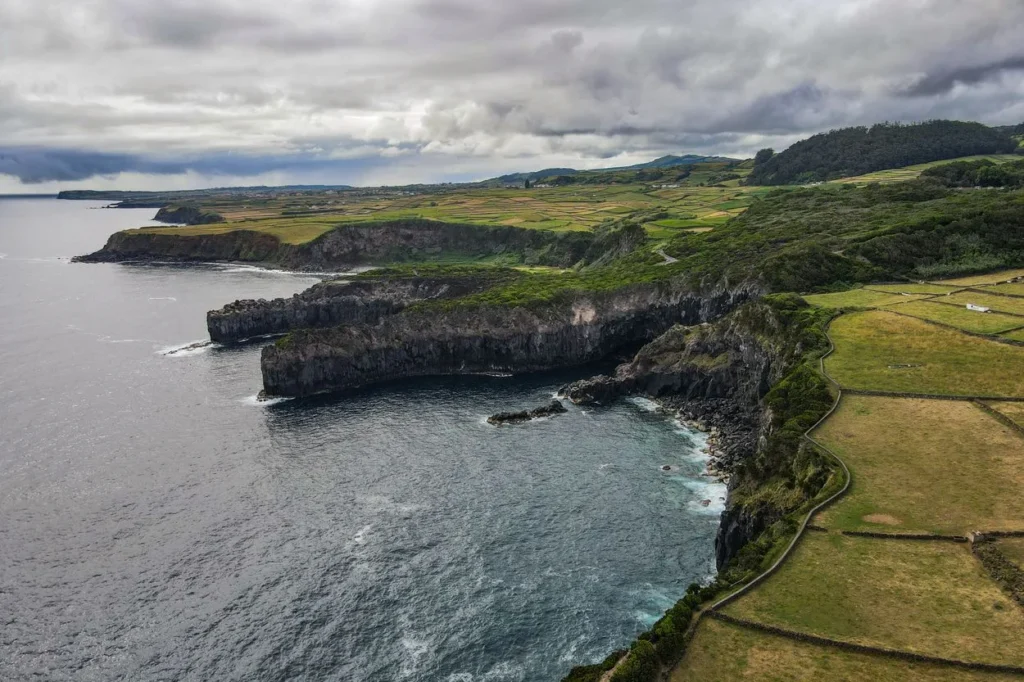 Aerial view of rocky volcanic cliffs and green patchwork fields along the Azores coastline