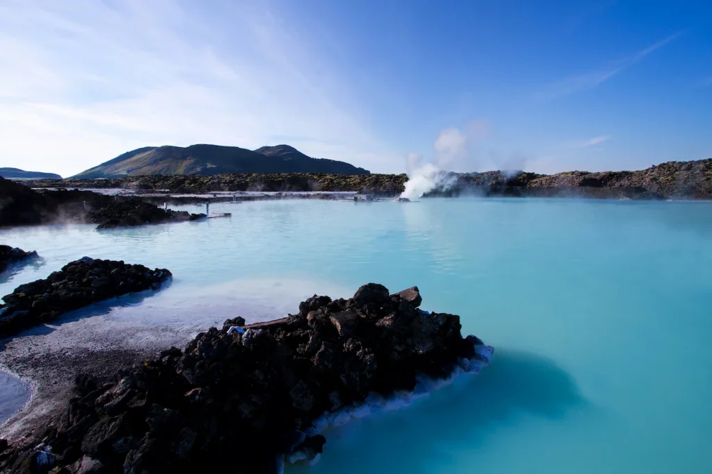 Geothermal spa with milky blue water surrounded by black lava rocks under a clear sky