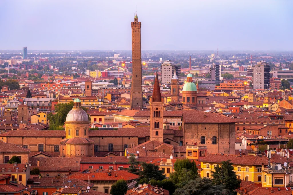 Elevated cityscape view of Bologna featuring the Asinelli Tower rising above red clay rooftops