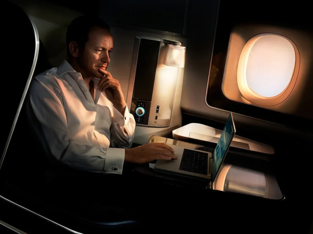 Businessman using a laptop next to an airplane window inside a dark cabin suite