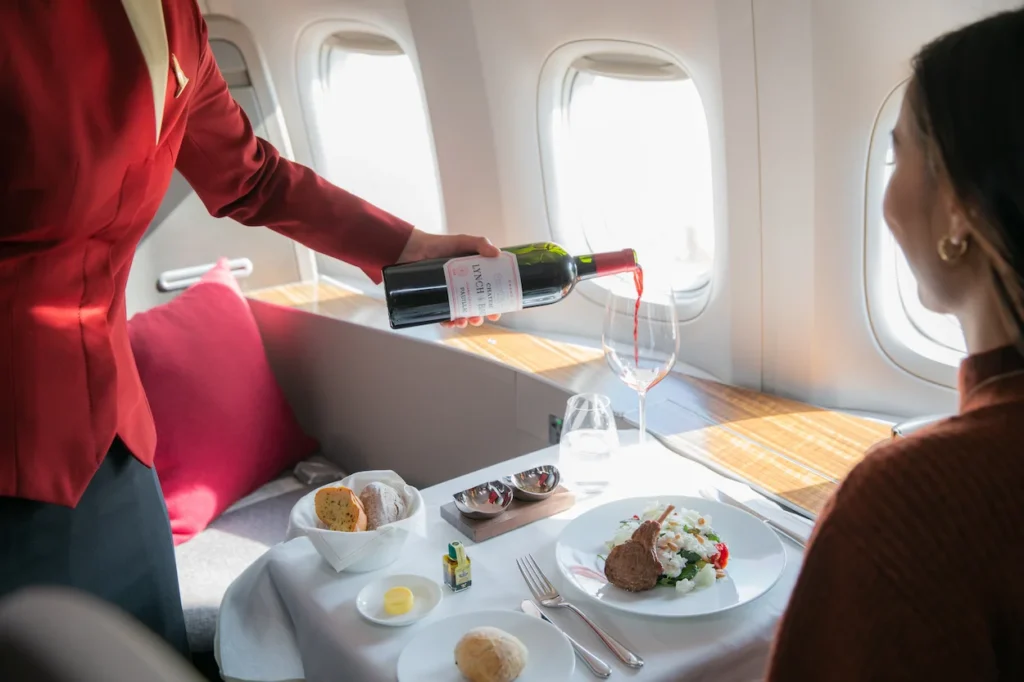 Flight attendant pouring red wine for a passenger during a First Class meal service on a Cathay Pacific flight