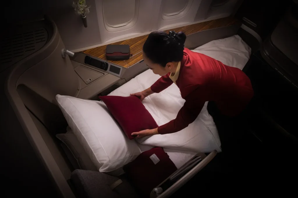 Flight attendant in a red uniform arranging pillows on a flat bed inside a luxury airplane suite