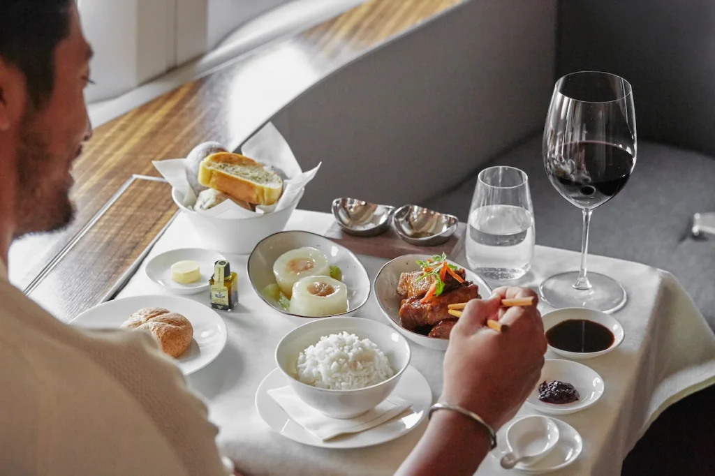 A passenger eating a luxury multi-course meal with chopsticks in a Cathay Pacific First Class suite