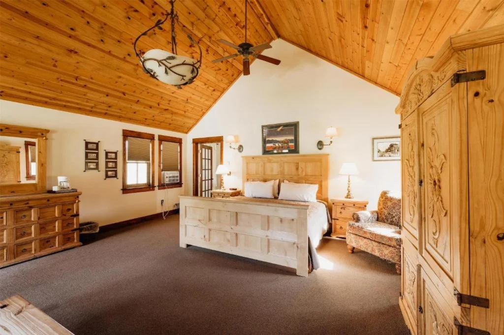 Rustic bedroom with a wooden bed frame, vaulted wood ceiling, and an armchair