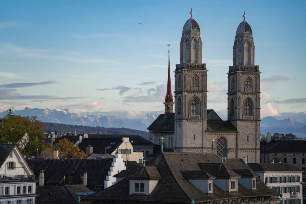 The twin towers of Grossmünster church in Zurich with snow-capped mountains in the background