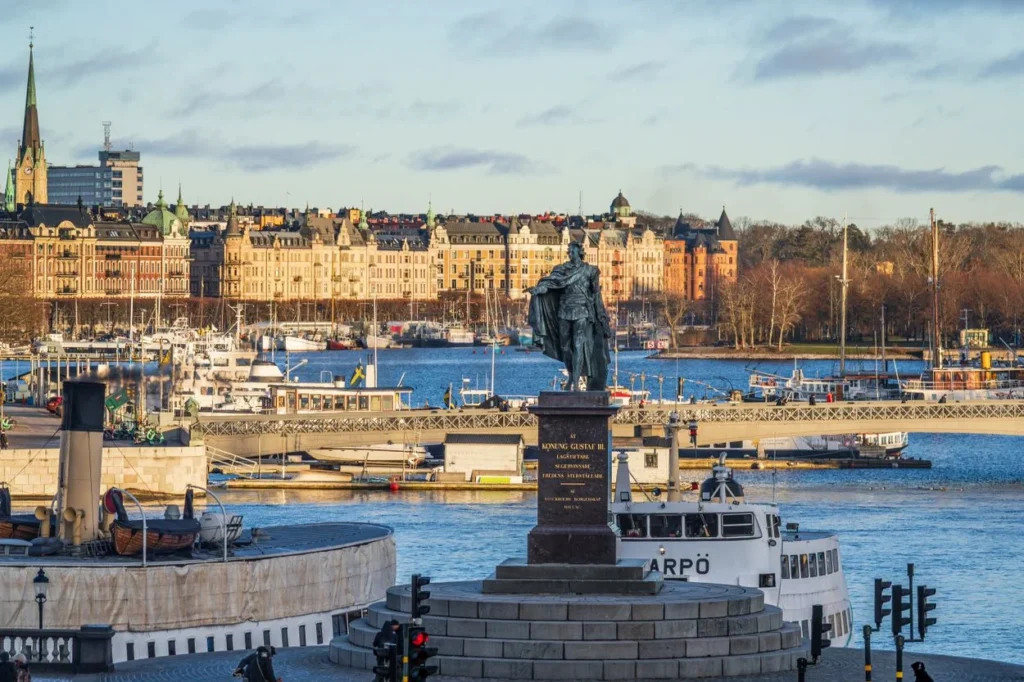 The bronze statue of King Gustav III overlooking a bustling Stockholm harbor under a bright sky