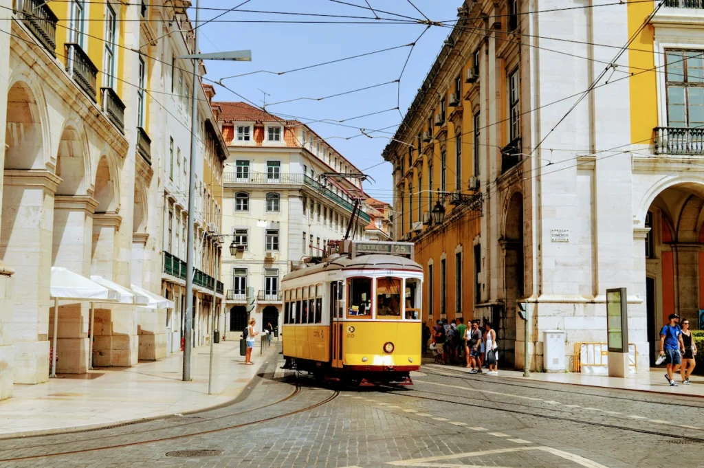A traditional yellow tram traveling down a cobblestone street bordered by historic yellow buildings in Lisbon