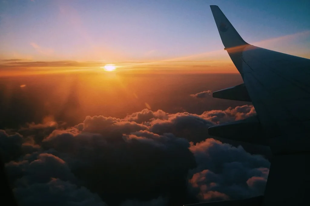 Malaysia Airlines airplane wing flying above clouds during sunset