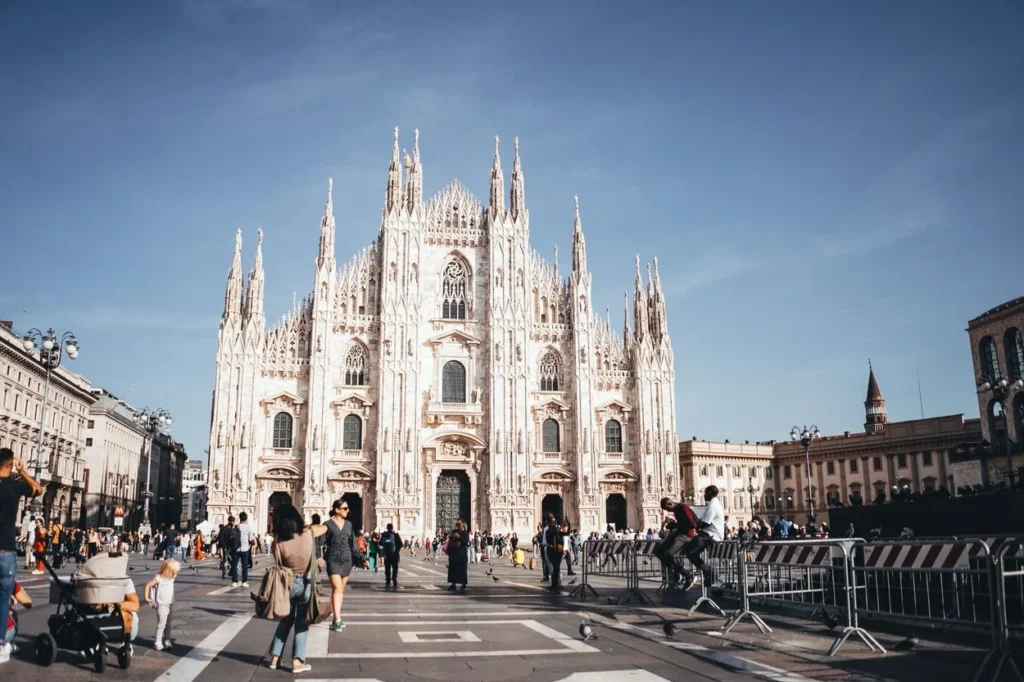 The white Gothic facade of the Milan Cathedral facing a busy public square