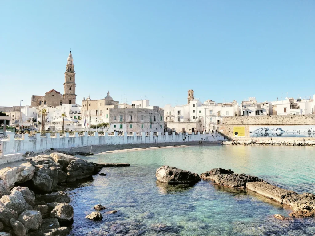 White stone buildings and church tower of Monopoli overlooking a sandy beach cove in Puglia