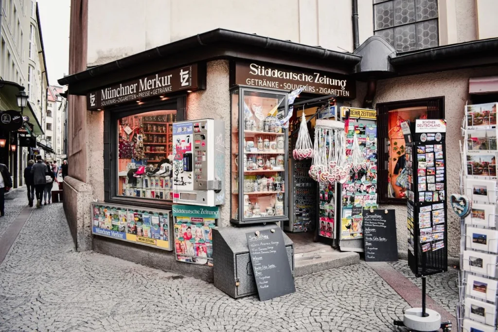 A street corner souvenir shop in Munich displaying postcards, mugs, and magazines