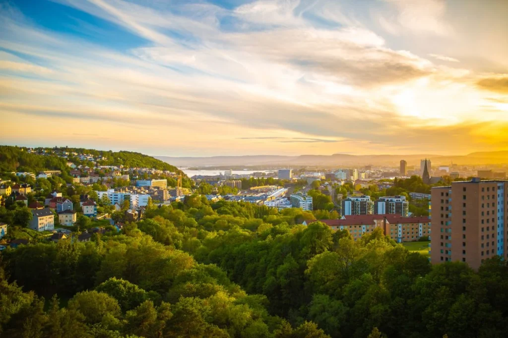 An elevated view of Oslo nestled in green hills under a bright sunset sky