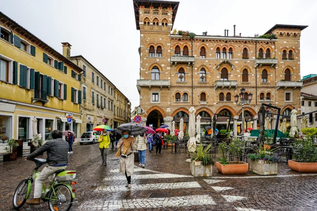Pedestrians with umbrellas and a cyclist in Piazza San Vito in Treviso, Italy