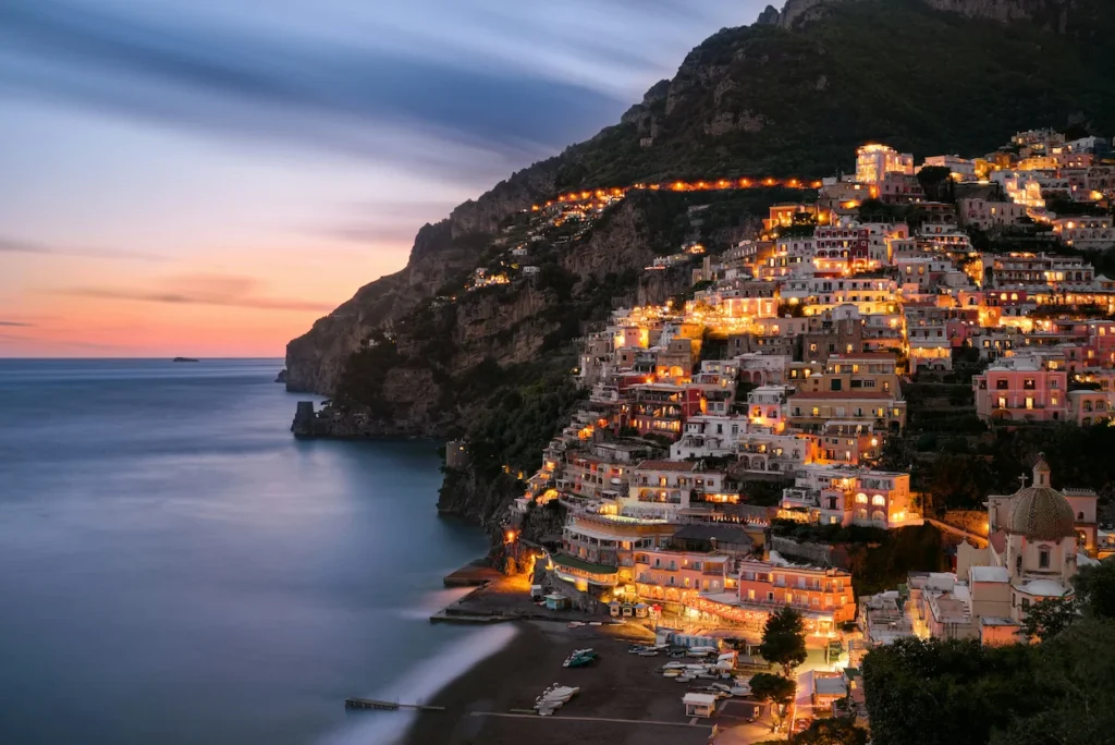 An evening view of Positano on the Amalfi Coast with glowing building lights overlooking the sea at sunset