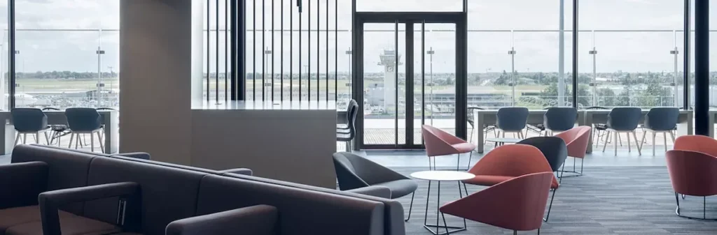 Modern airport lounge with colorful armchairs and floor-to-ceiling windows showing the tarmac