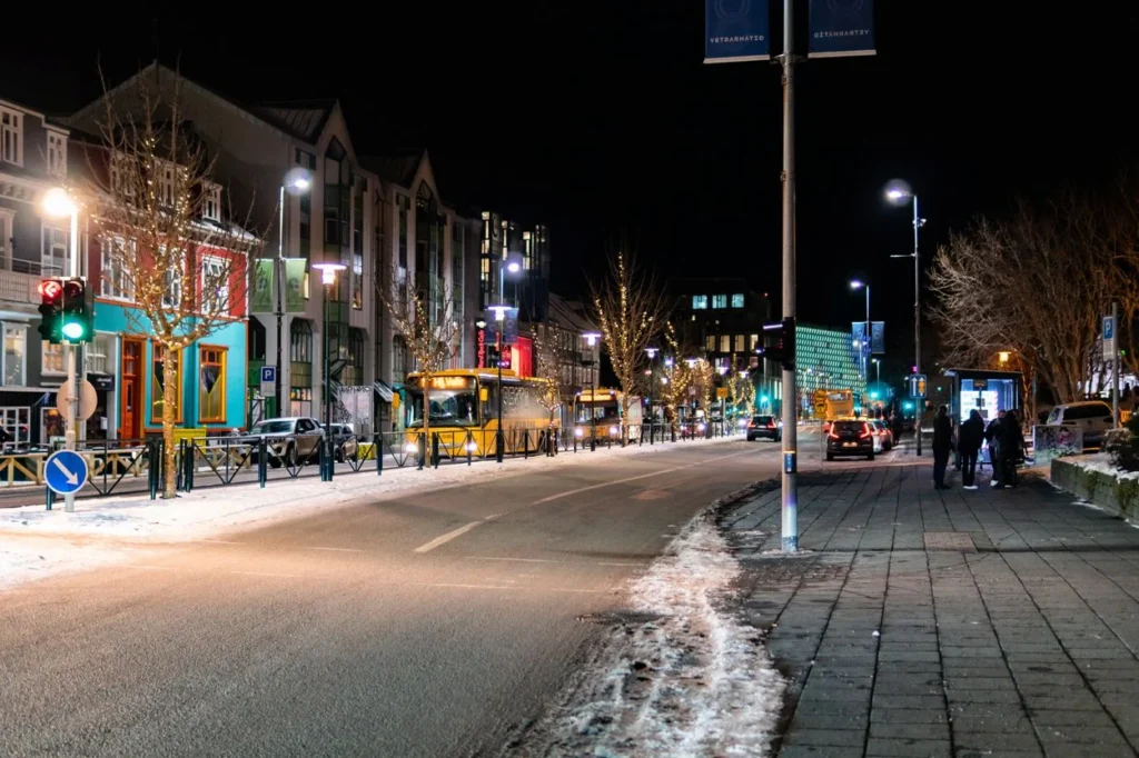A snowy Reykjavik street at night with yellow city buses, streetlights, and buildings