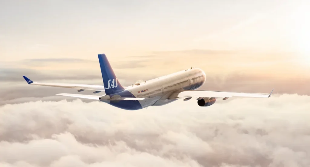 An SAS airplane flying above a sea of thick white clouds during sunset