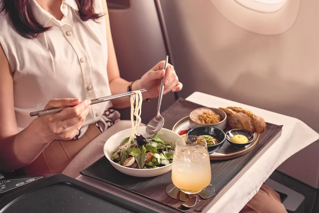 Passenger using chopsticks to eat noodles and side dishes from an airplane tray table