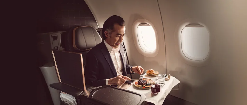 Man in a suit eating a steak meal inside a Starlux Airlines business class seat by the window