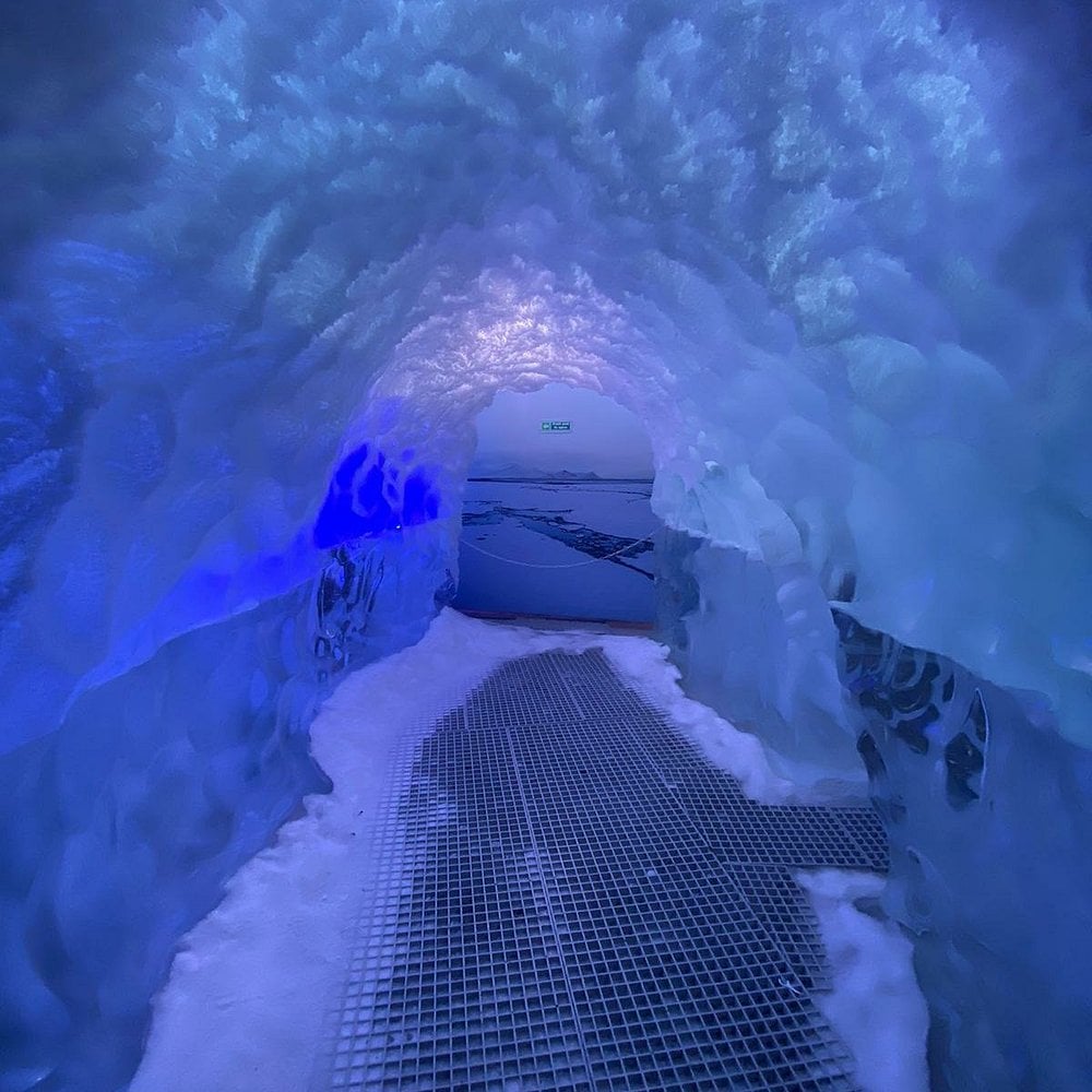 Icy blue tunnel at Perlan with textured snow walls and a grated walkway.