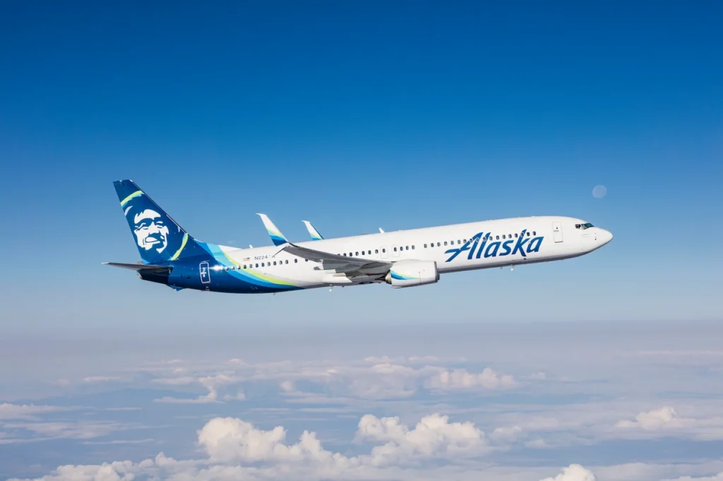 An Alaska Airlines passenger airplane flying high above a layer of fluffy white clouds