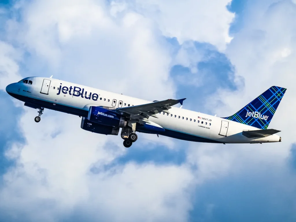 A JetBlue passenger airplane flying upward into a cloudy blue sky