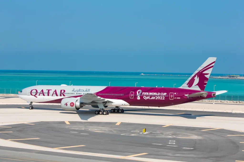 Qatar Airways passenger airplane featuring a maroon FIFA World Cup livery parked on the tarmac near water