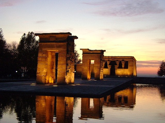 Templo de Debod illuminated at sunset with reflections in the water.