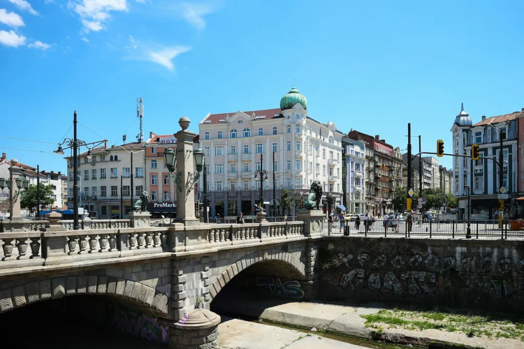 The historic stone Lions Bridge in Sofia, Bulgaria, with city buildings and a clear blue sky in the background