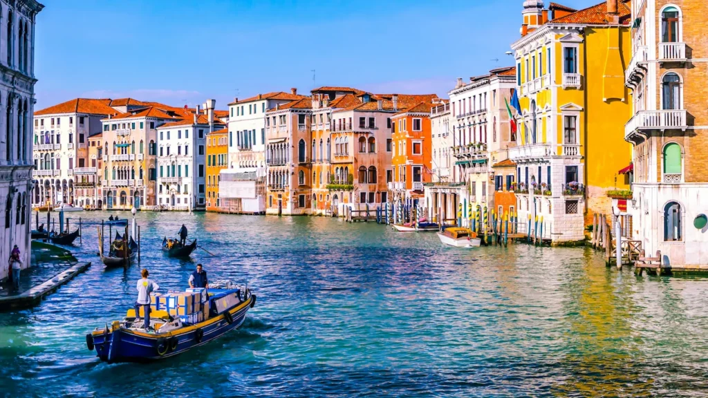 A utility boat and gondolas navigating the Grand Canal in Venice, Italy, lined with colorful historic buildings
