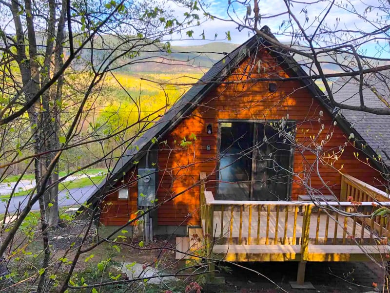 This charming A-frame cabin is surrounded by trees, providing the perfect backdrop for your autumn escape