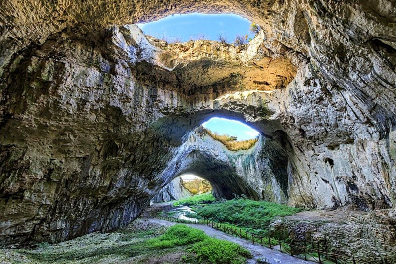 View of Devetashka Cave in Bulgaria, featuring its vast entrance and lush green surrounding