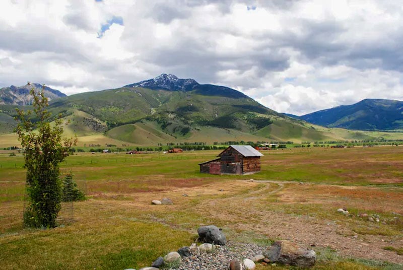 Elk Ridge Cabin in a vast meadow with mountain views under a cloudy sky.