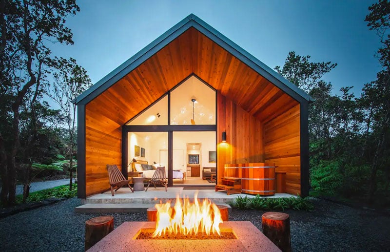 Image showing a modern cabin at Kūono at Volcano with wood accents, glass doors, and a fire pit in a forest.