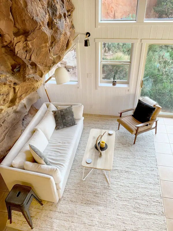 A bright living room with a natural rock wall, large windows, and minimalist decor in the Sage Canyon Cliff House.