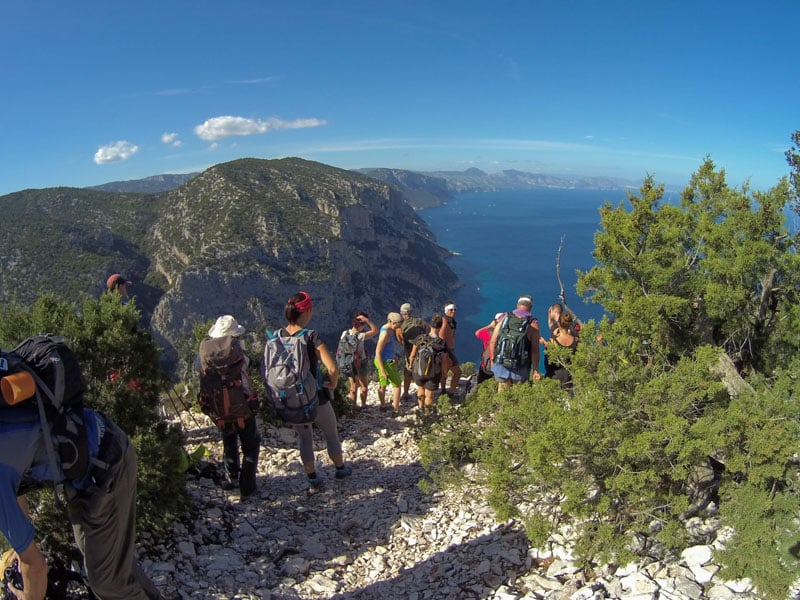 Hikers navigate the Selvaggio Blu trail during the day, surrounded by rugged cliffs and the stunning Sardinian coastline.
