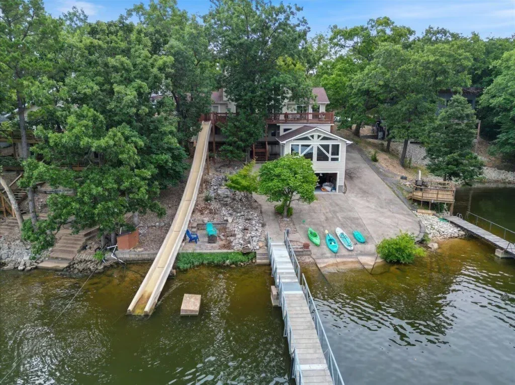 Aerial view of a lakefront house with a long water slide extending from the deck down to the lake