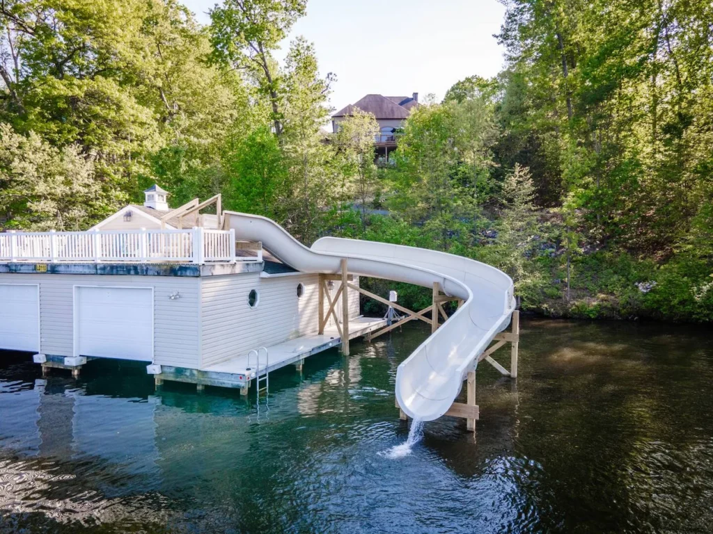 Two-slip boathouse with a large white curving water slide dropping into a lake