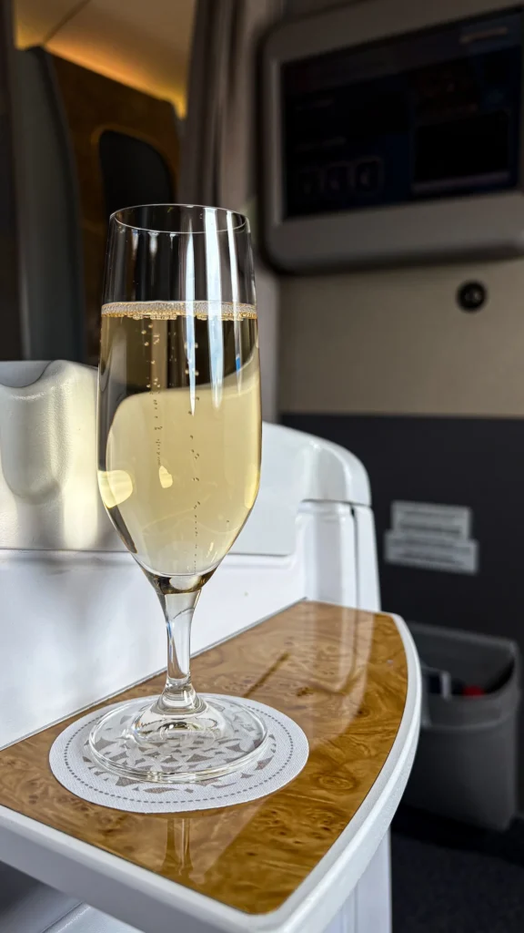 Glass of sparkling champagne on a wooden side console inside an Emirates business class cabin
