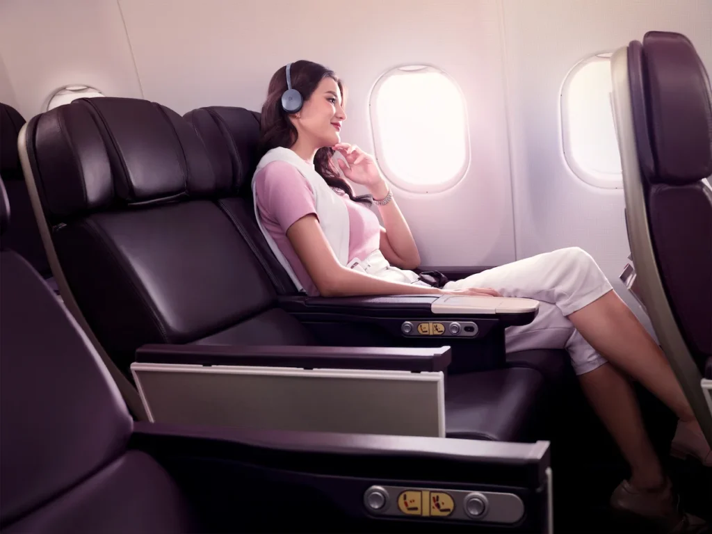 A passenger wearing headphones in a purple leather Thai Airways premium economy seat