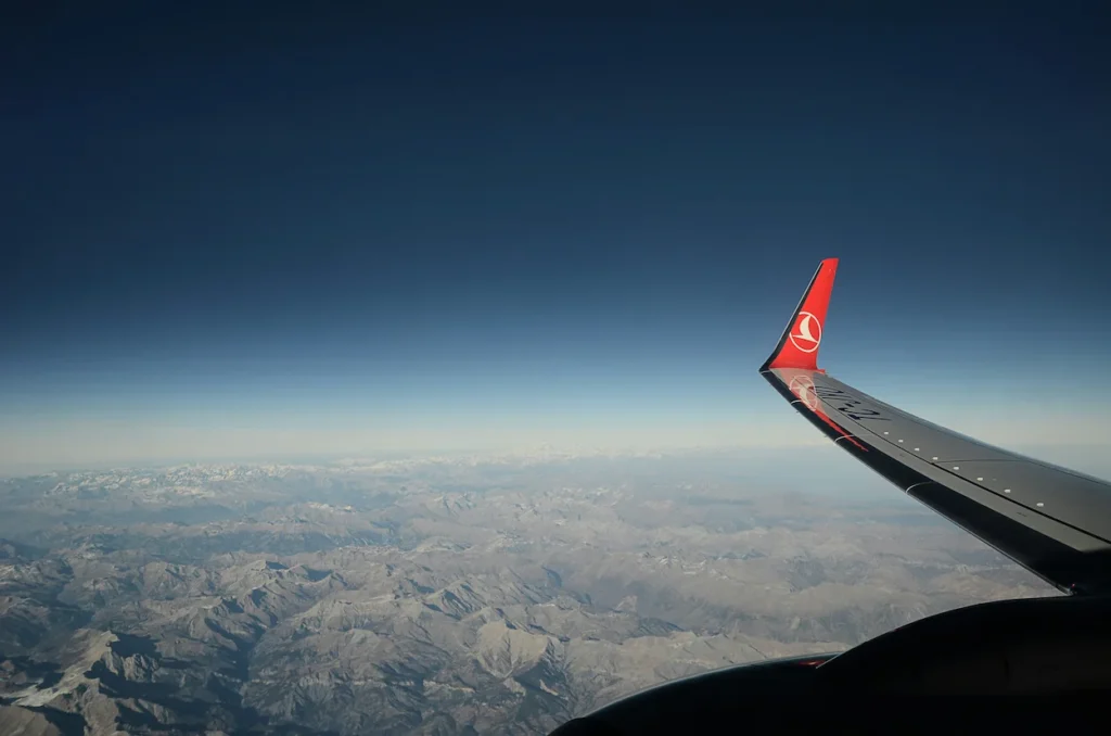 Turkish Airlines winglet tip flying over a rocky mountain landscape under deep blue sky